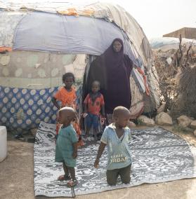 Eine Frau steht mit einigen Kinder vor einer behelfsmäßigen Hütte
